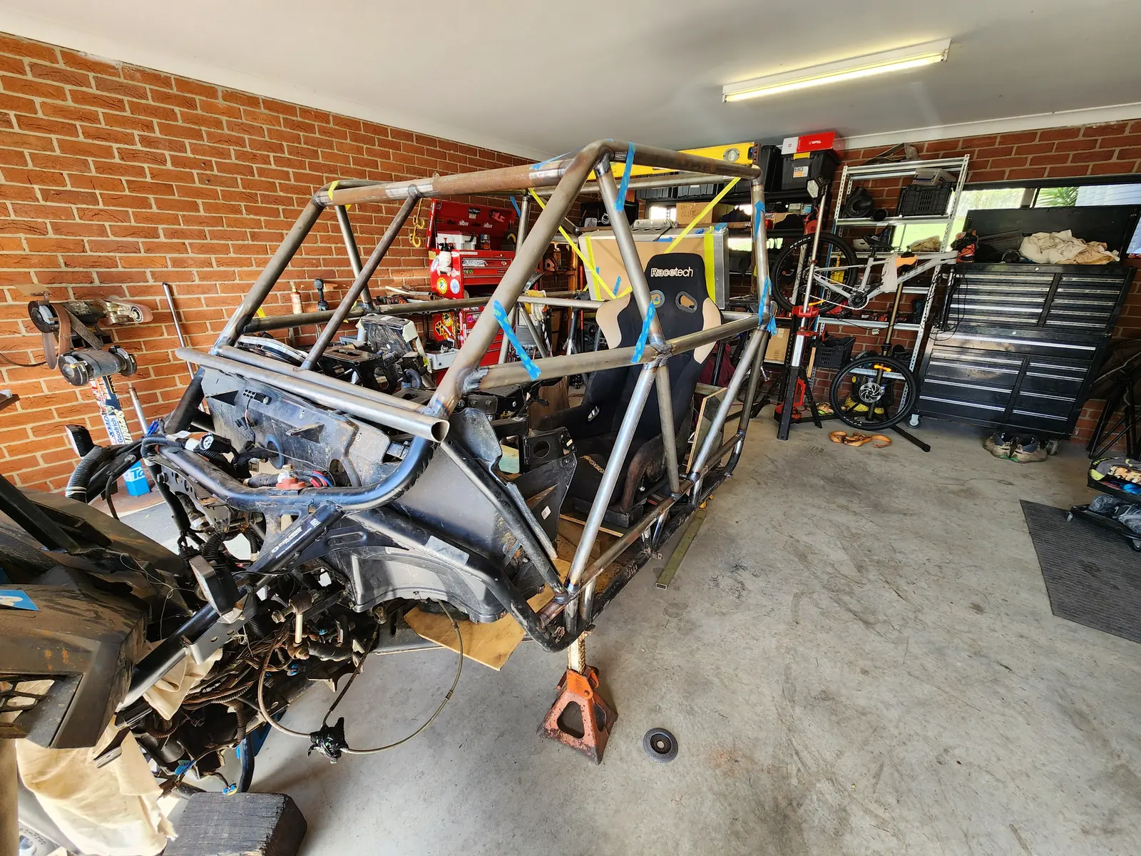 Bare steel tube chassis on stands in a home garage, drivetrain sitting inside the frame