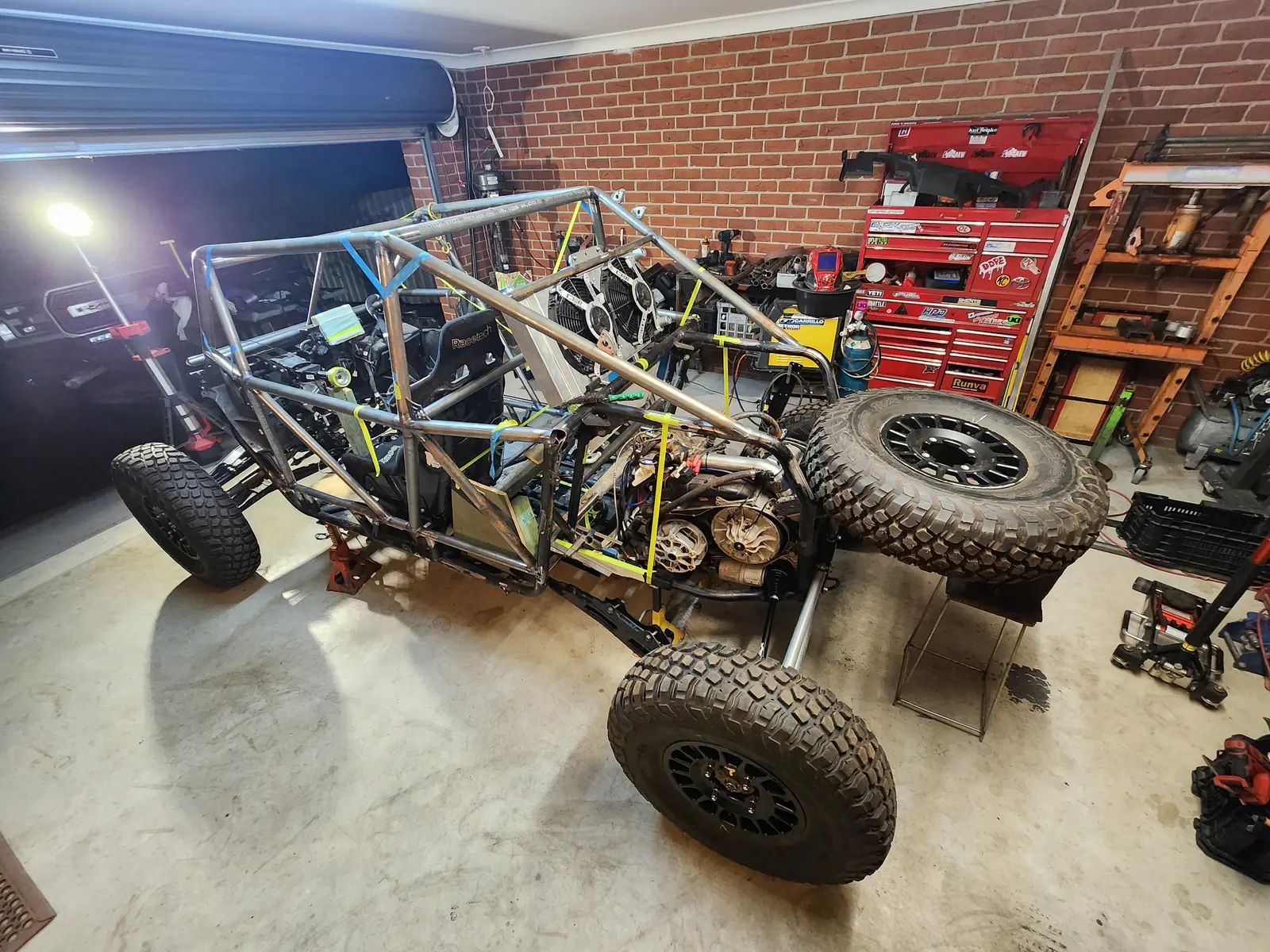 Tube chassis sitting on off-road tyres with suspension fitted, in the garage at night
