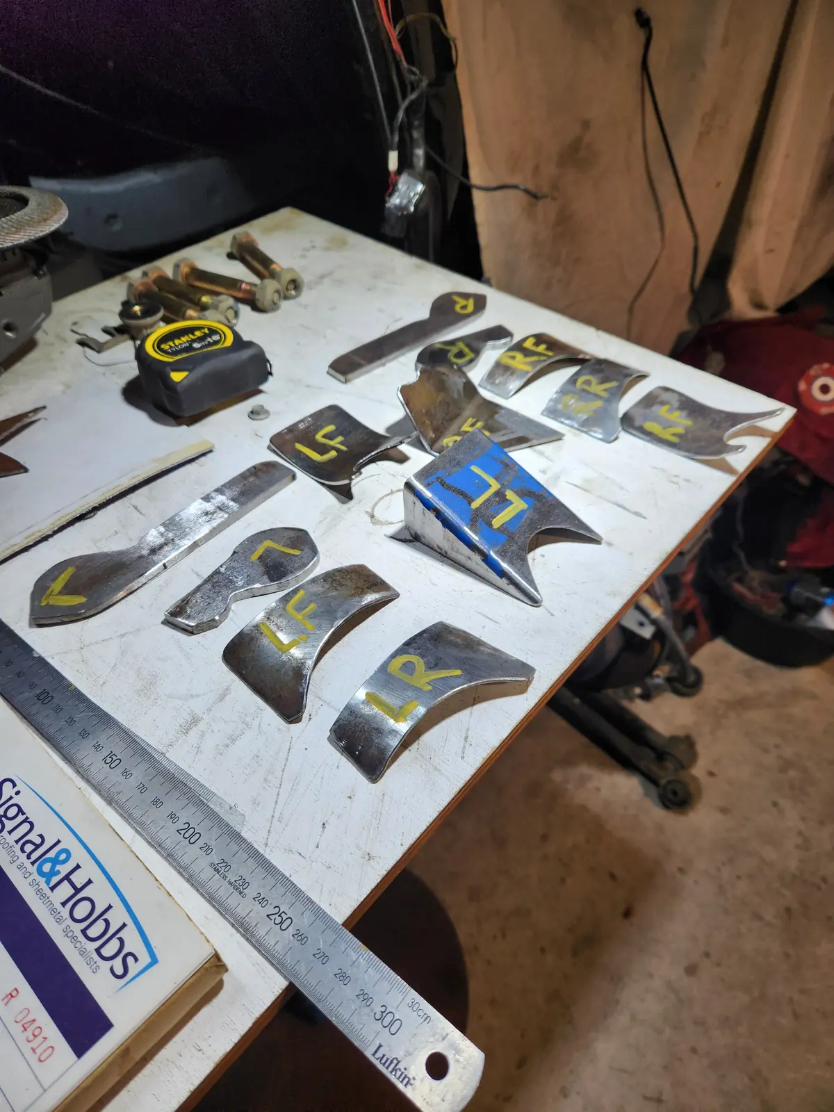 Steel plates cut to shape and labelled for each corner on a work table