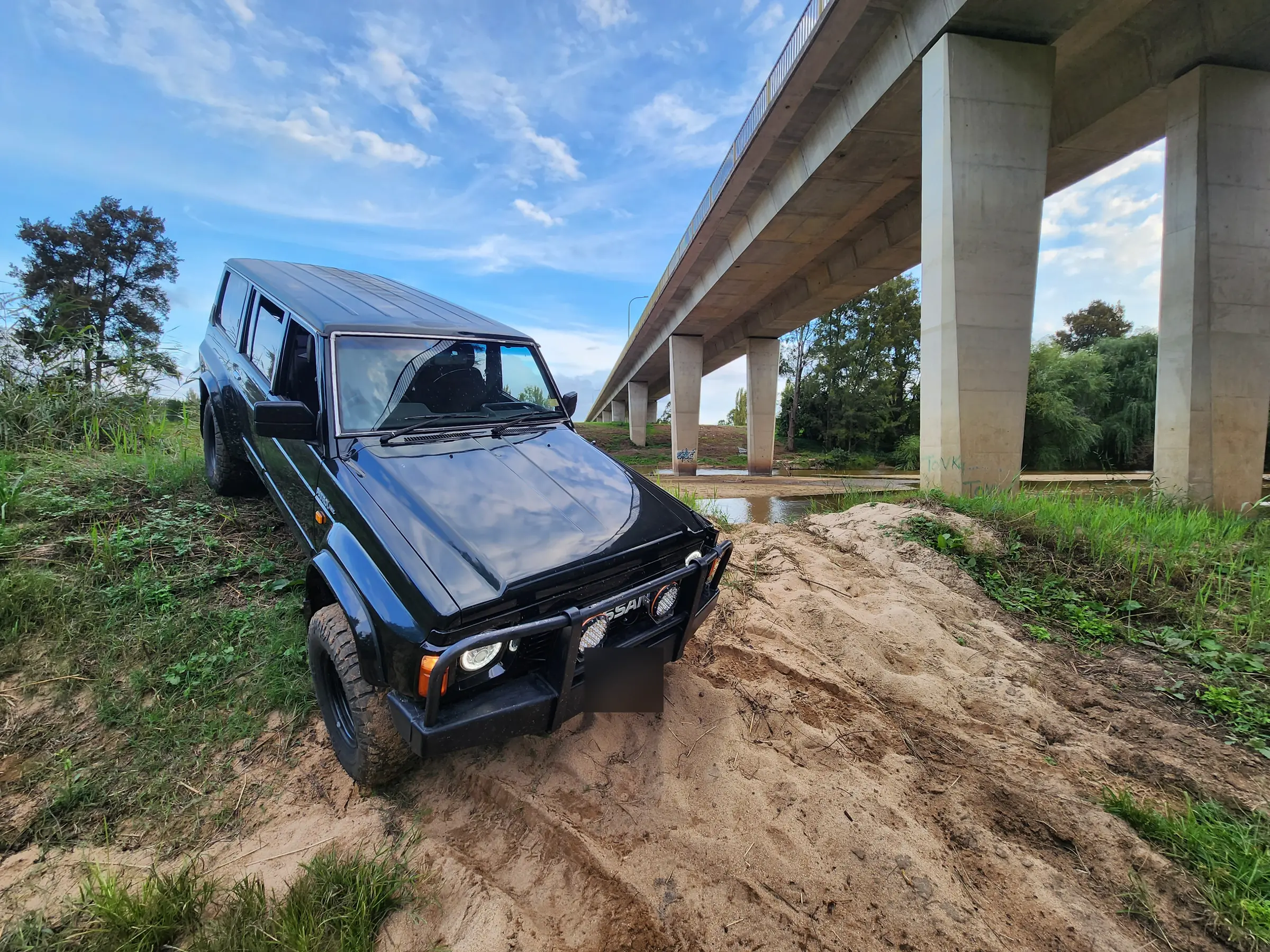 Black Nissan GQ Patrol wagon climbing a sandy bank under a concrete bridge